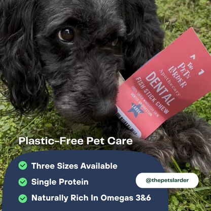 Dog holding a red dental chew treat with text about plastic-free pet care on a grassy background.